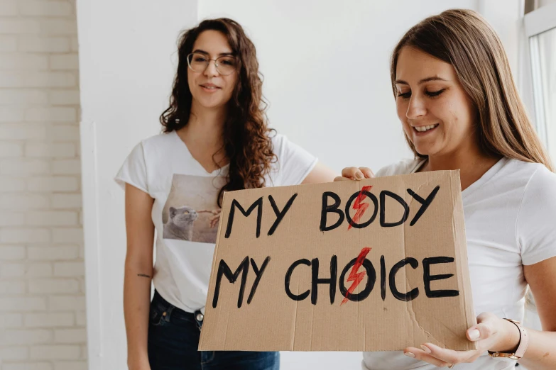 two women are holding a cardboard sign that says my body is my choice