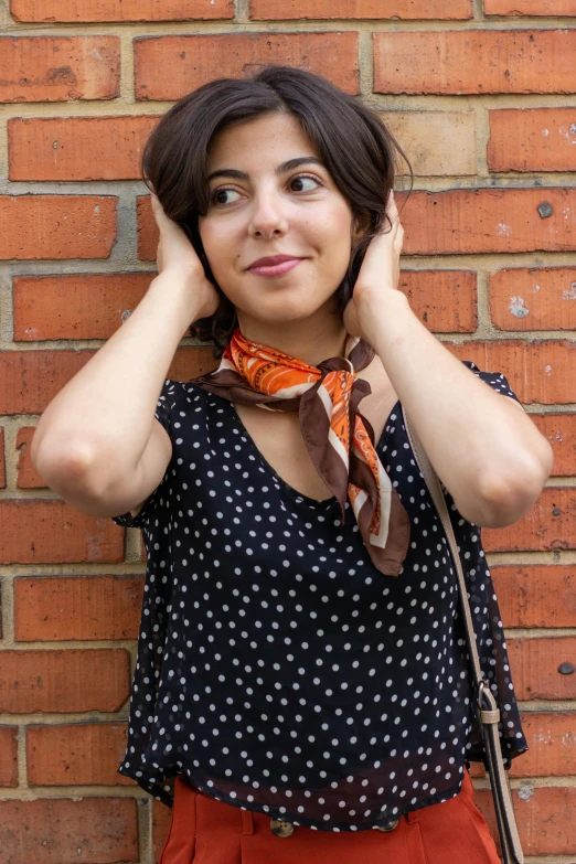 a woman in black and white shirt holding her head near brick wall