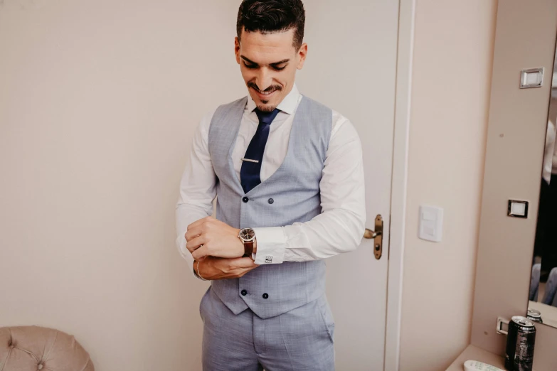 a man in a light blue suit is putting on his tie