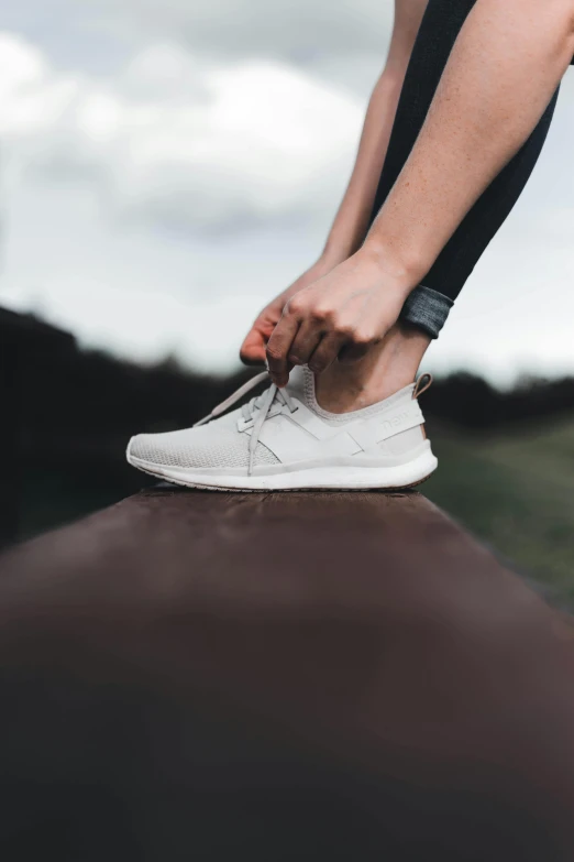 a person tying the shoelaces of a white tennis shoe