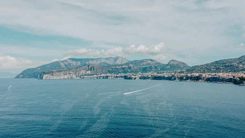 blue water with waves going to shore and mountains around it