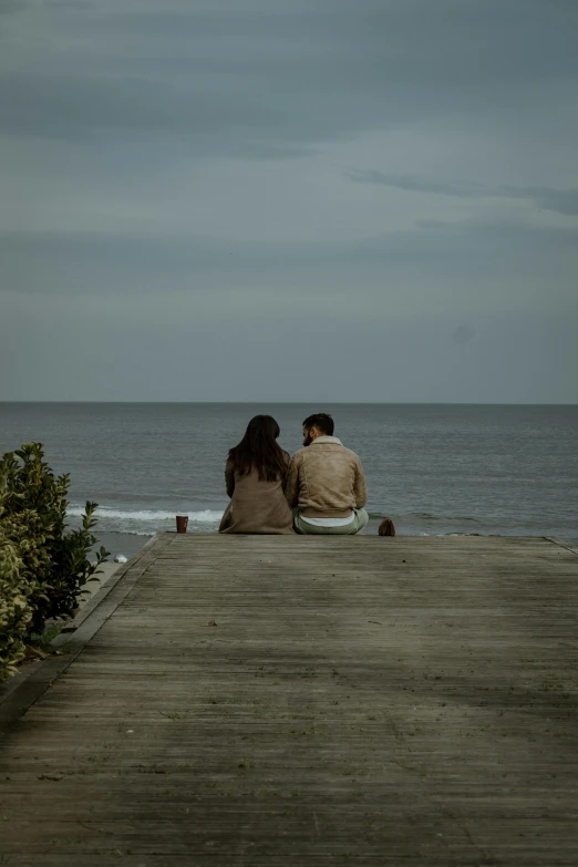 a couple is sitting on the dock facing the water