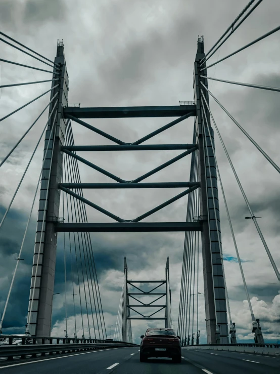 car driving across a large metal bridge on a cloudy day