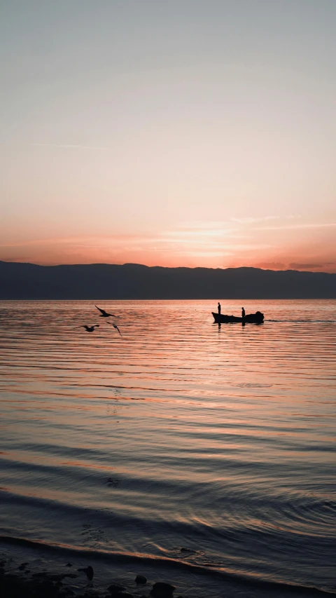 two men paddling in small boats out into the sea at sunset