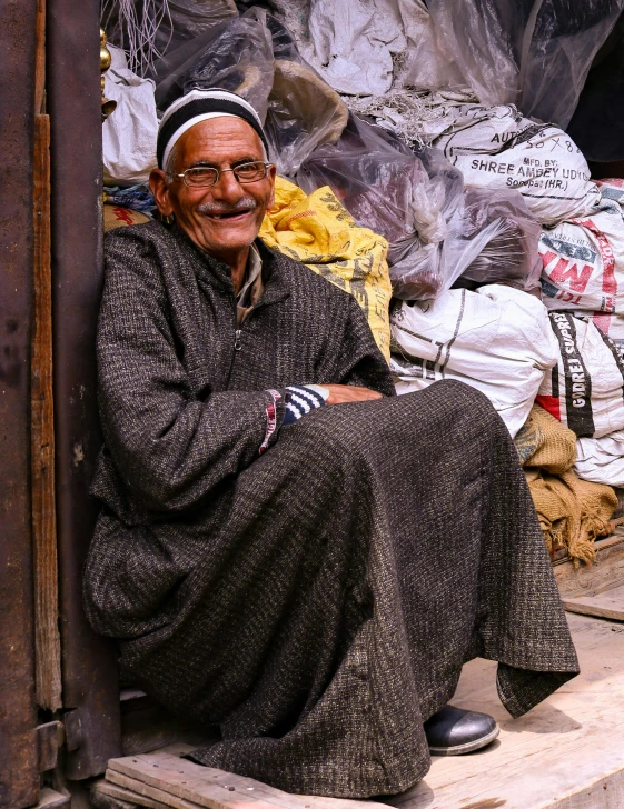 the old man sits in front of the shop selling a variety of stuff