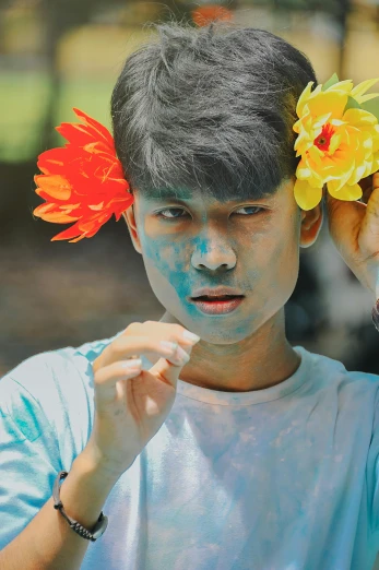an asian man with blue and yellow face paint holding flowers in his hair