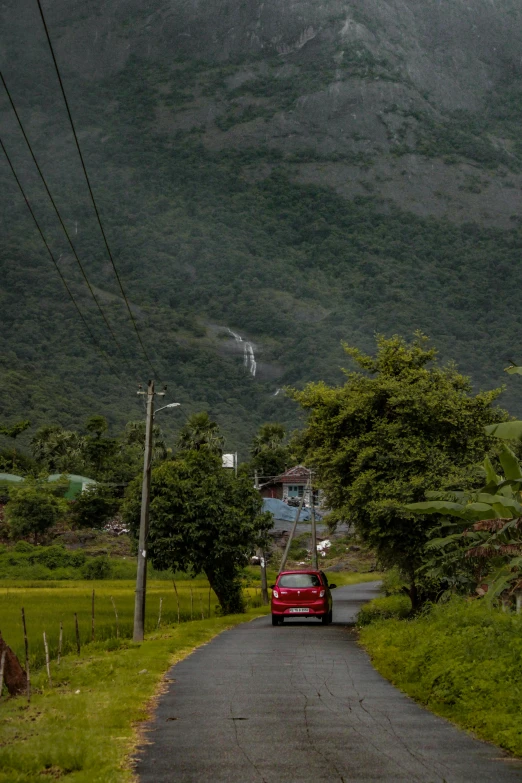 red car driving on a road in a green mountainside with power lines above