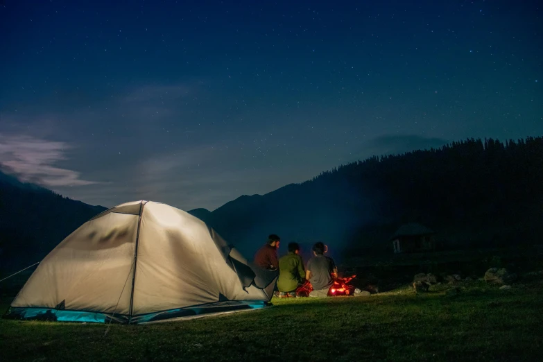 people stand near a tent while camping under a night sky