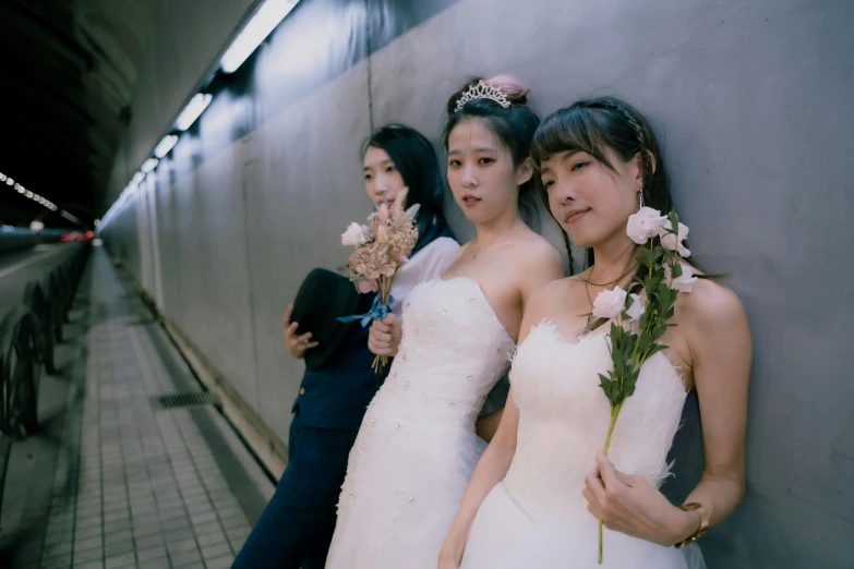 three women in white dresses leaning against a wall