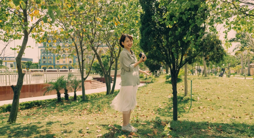 a woman standing in the grass near some trees