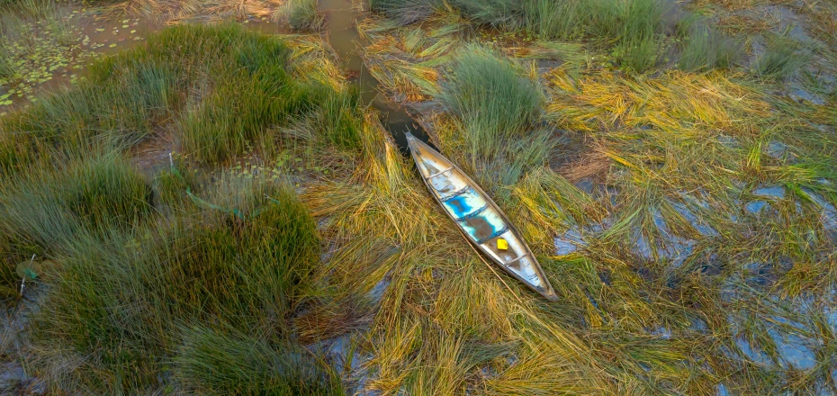 a broken kayak on dry ground with weeds