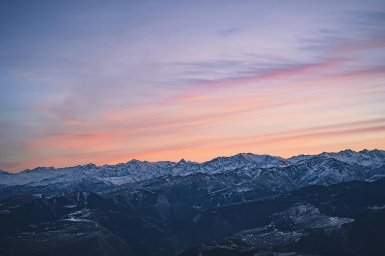 a view of snow - capped mountains and the sky at dusk