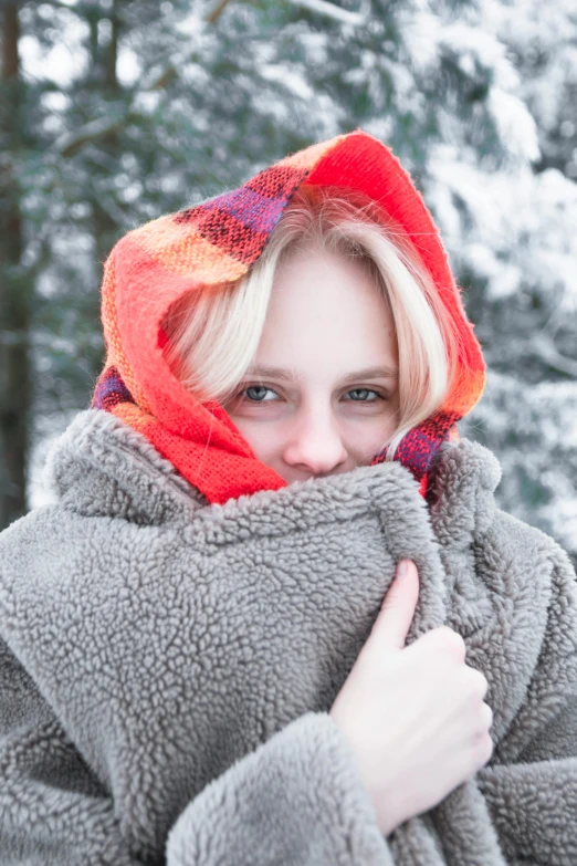 a woman in grey coat wrapped around winter tree