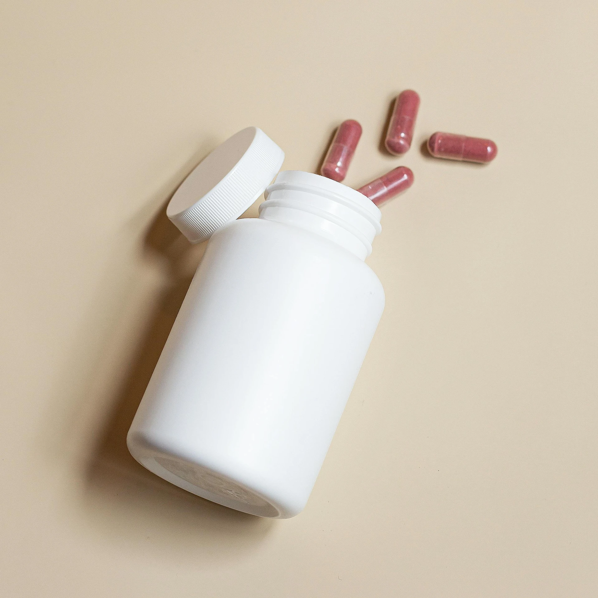 pink pills spilling out of a bottle on a beige background