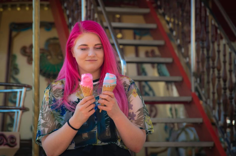 a girl with pink hair sitting holding two ice cream cones