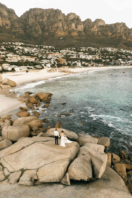 a couple stands on some rocks by the beach