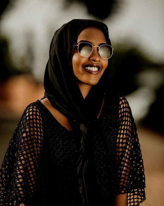 a woman wearing a scarf and shades smiles at the camera