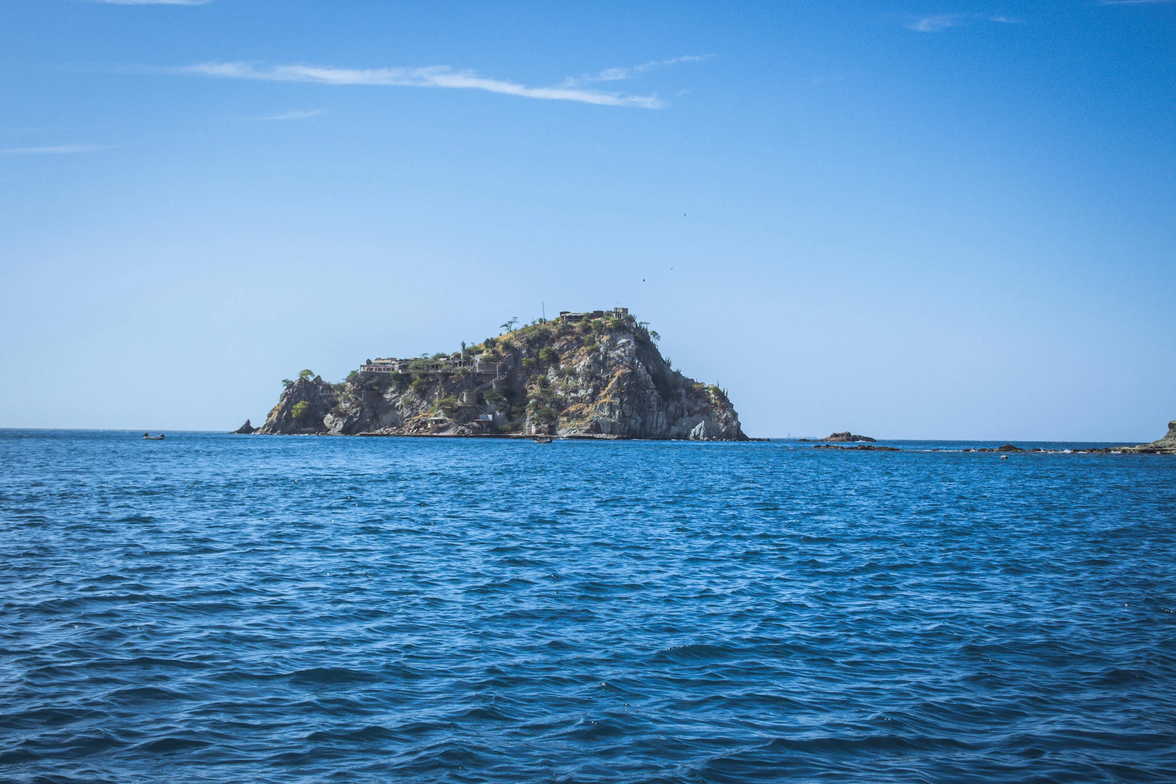 an island is surrounded by blue water and blue skies