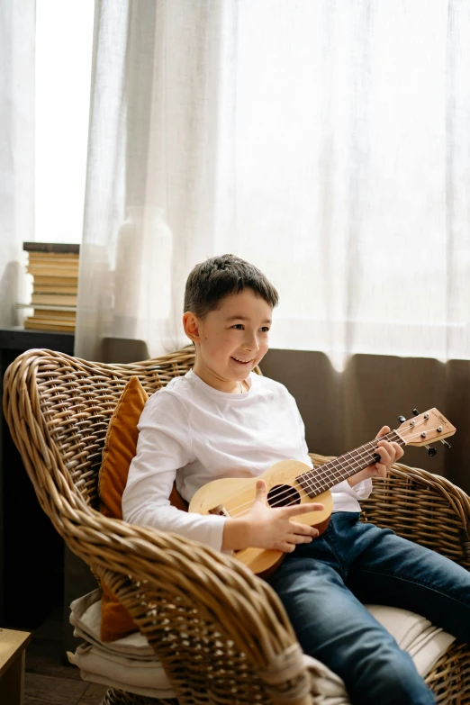 a small boy playing the guitar while sitting in a chair