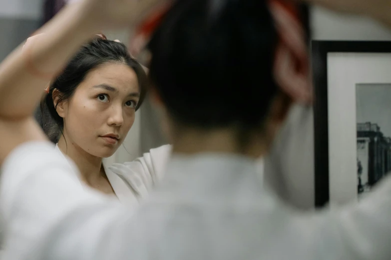 an asian woman combs her hair while looking into the mirror