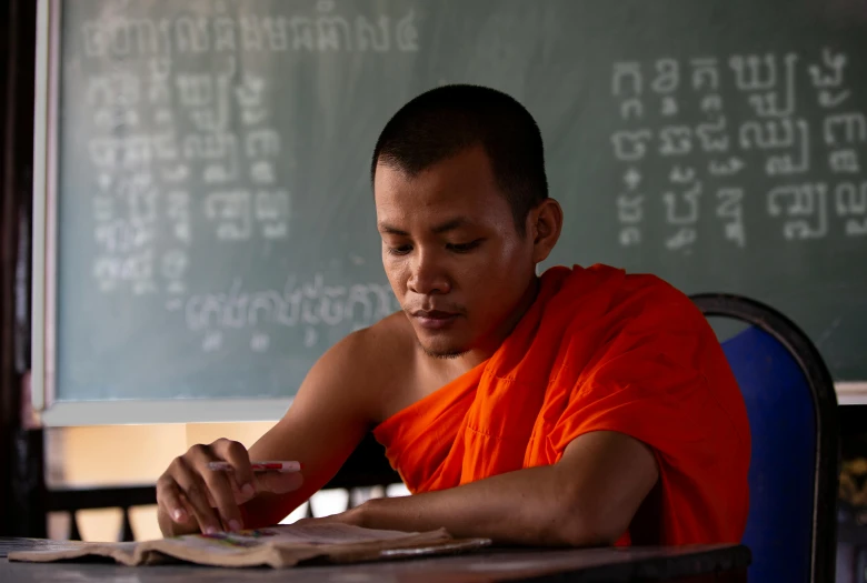 a man in a orange shirt and some writing on a blackboard