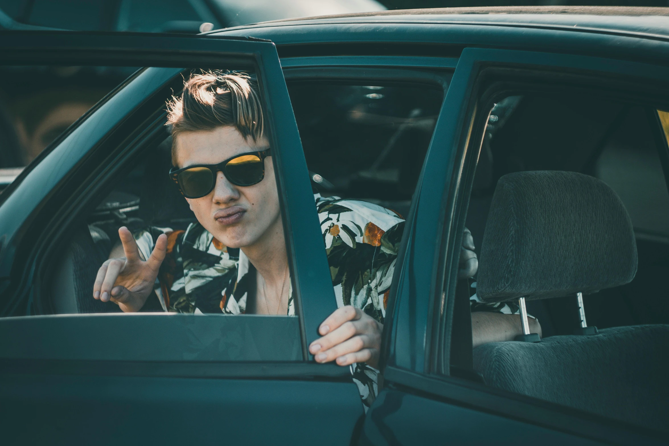 man with sunglasses sticking his finger out the car window