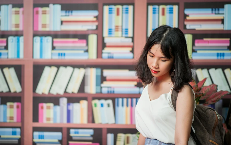 a woman looks down while standing in front of bookshelves