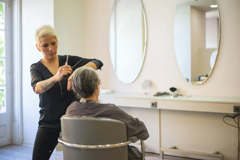 a woman blow dries another woman's hair in front of a mirror