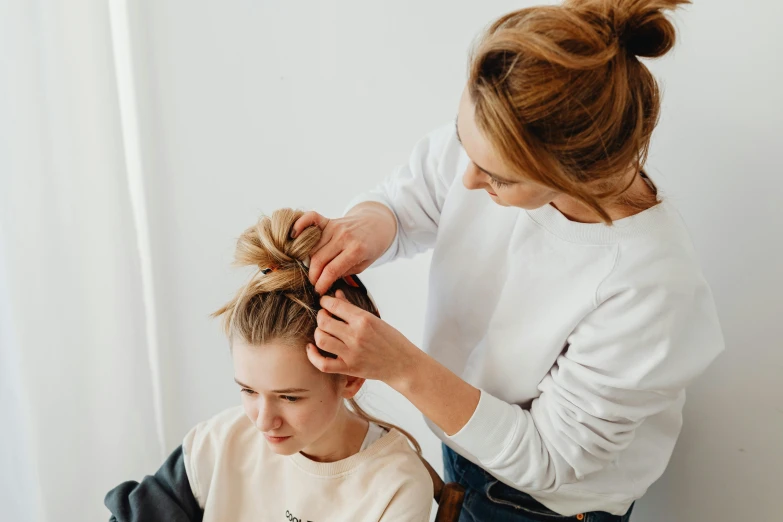 a girl is getting her hair styled by a woman
