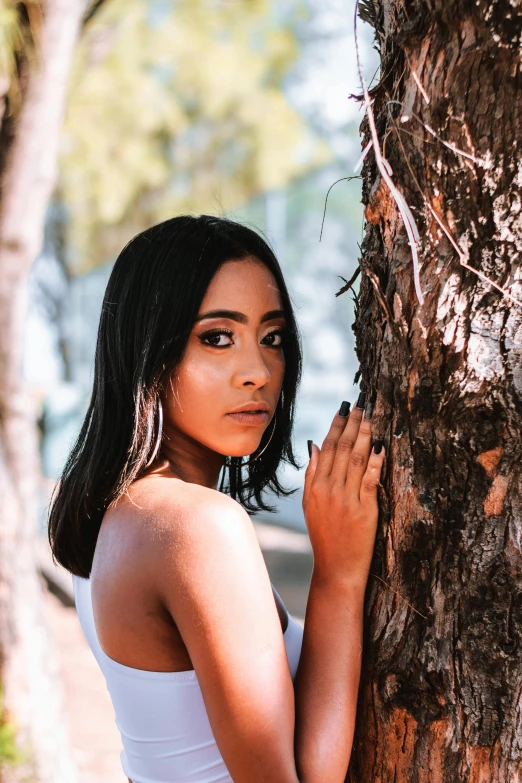 a beautiful woman leaning on a tree trunk