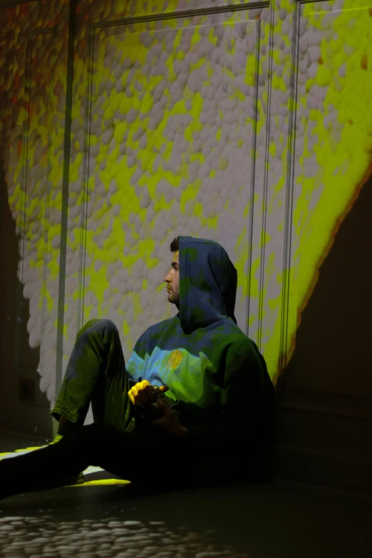 a man sitting on the floor wearing a hooded coat