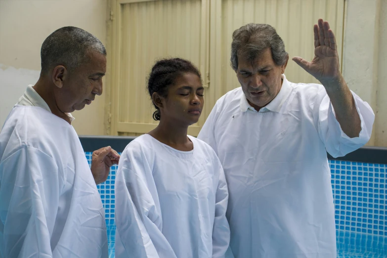 two people wearing white clothes are standing near a pool and another is holding his hands up