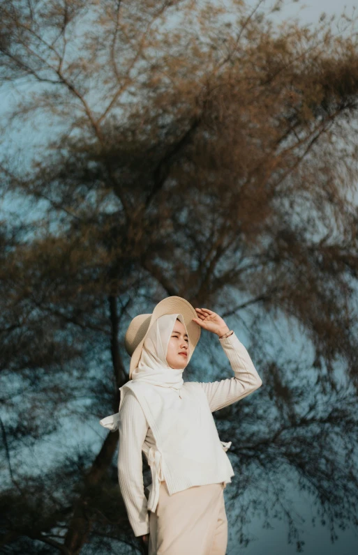 a woman in hijab and a hat standing near trees