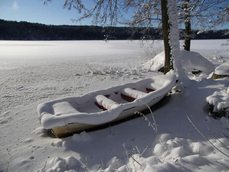 a wooden boat buried in snow by a tree