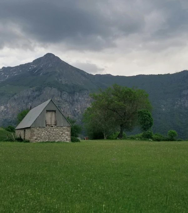 a stone barn sitting in a large field under a mountain range