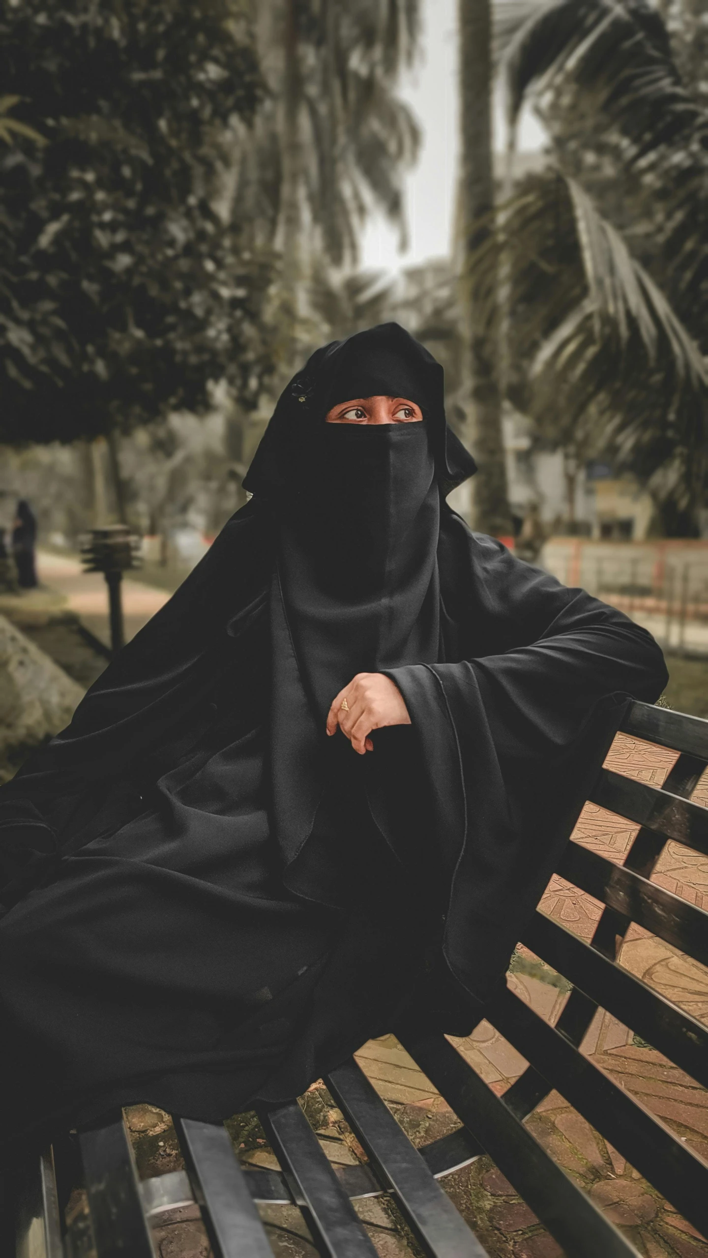 a woman wearing a black veil is sitting on a park bench