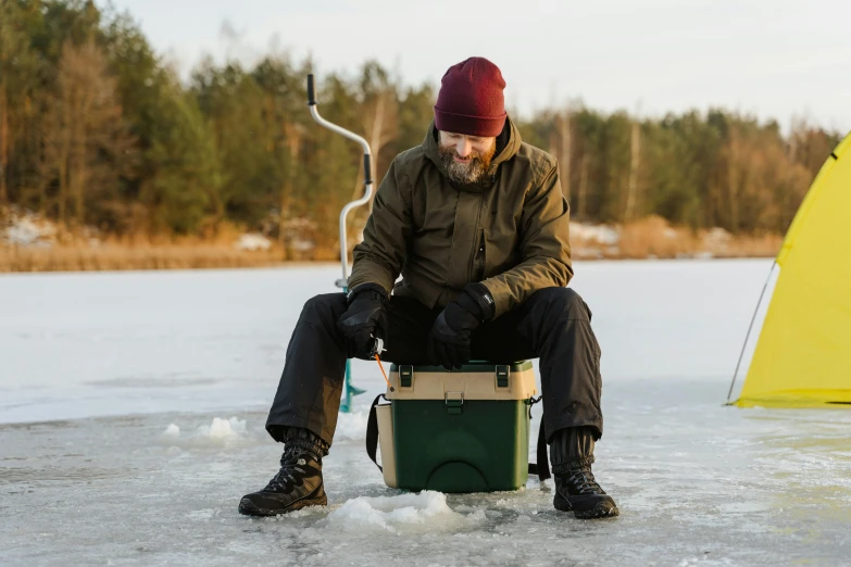 a man in brown jacket ice fishing with yellow tarp