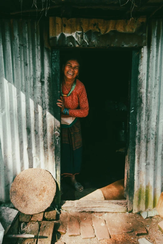 a woman smiles out from the doorway of her hut