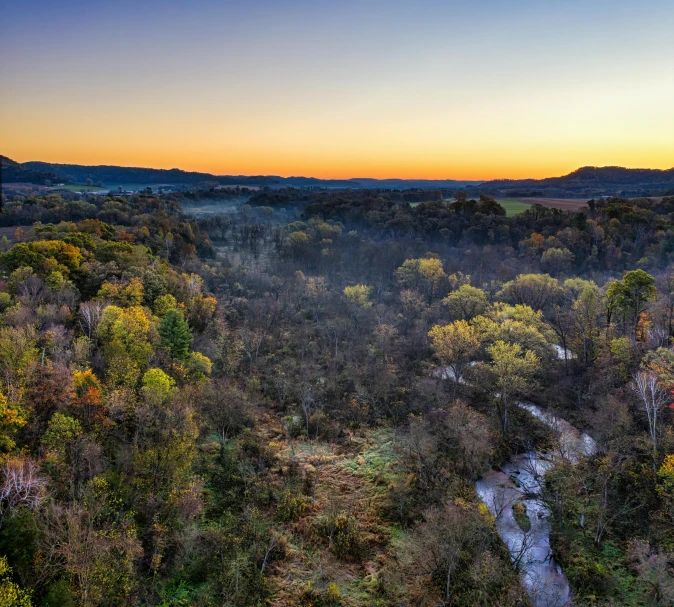 the sun rises over a beautiful tree covered valley