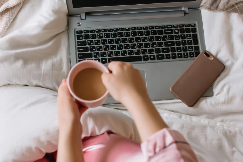 a woman in bed with a laptop and a coffee mug