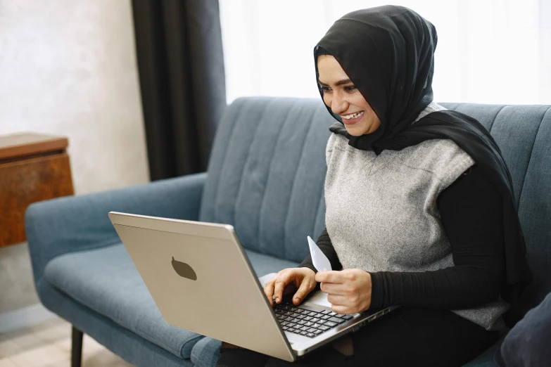 a woman wearing a hijab sitting on a couch and using a laptop