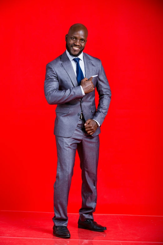 man in grey suit standing on red wall holding a cellphone