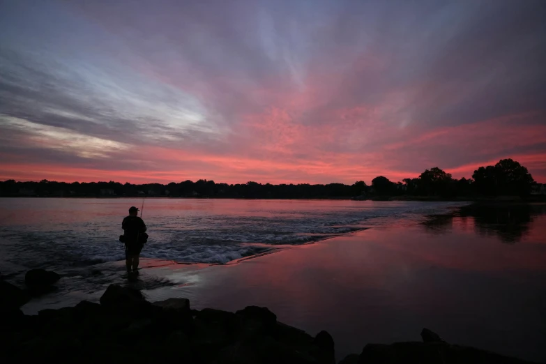 silhouette on beach next to body of water with cloudy sky