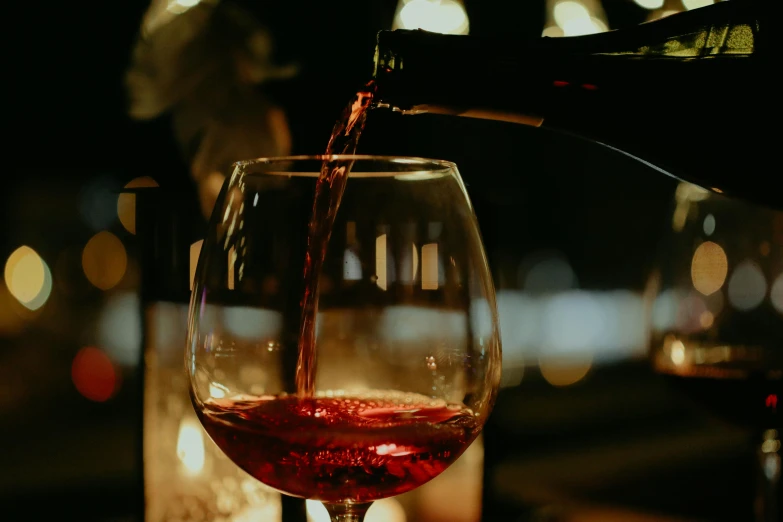 red wine being poured in a glass with boke of blurry lights behind it