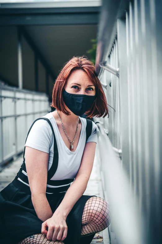 a young woman sits on a railing wearing a mask