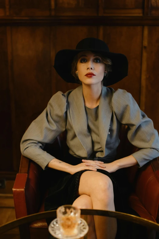 a woman wearing a black hat and gray dress sitting on top of a chair