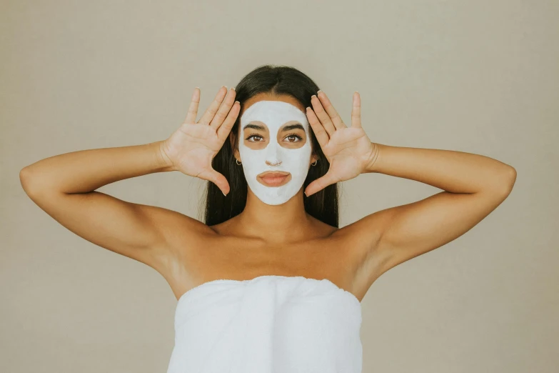 woman with facial mask on and her hands over her head