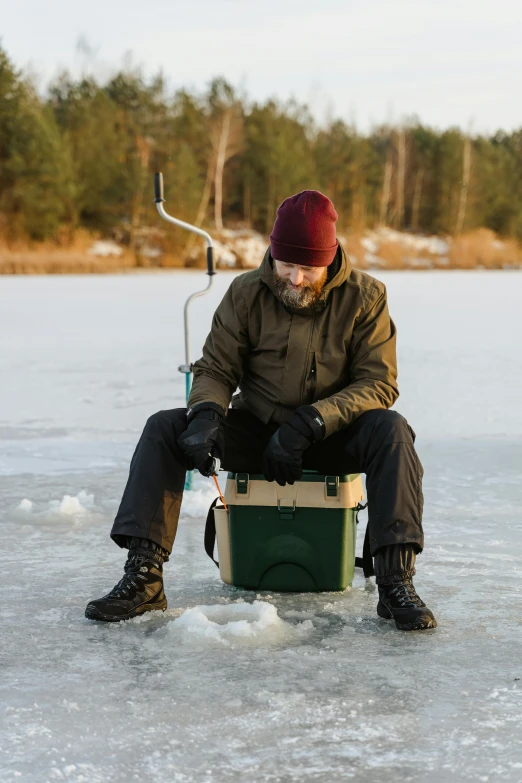 the man is sitting on the ice with a small fishing basket