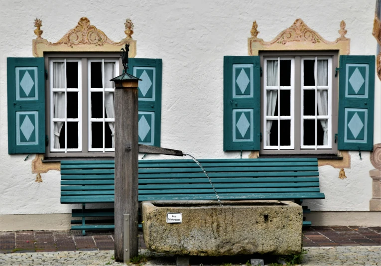 a green bench sitting by a wooden pole in front of two windows