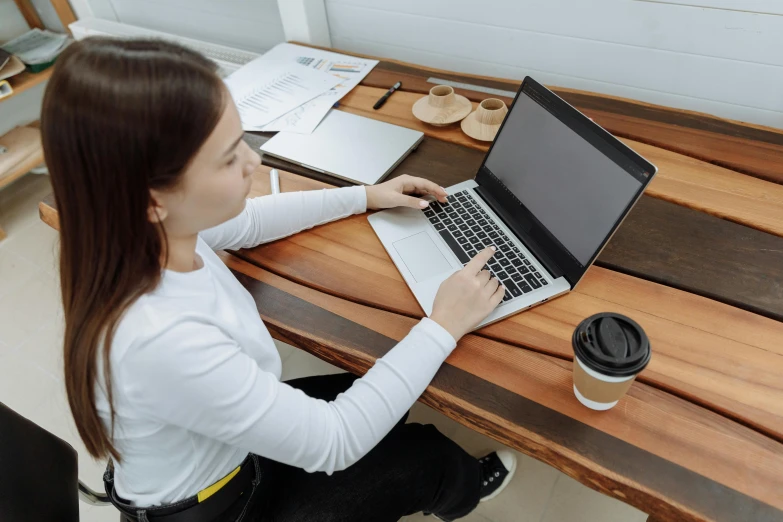 the woman is using her laptop on the wooden table